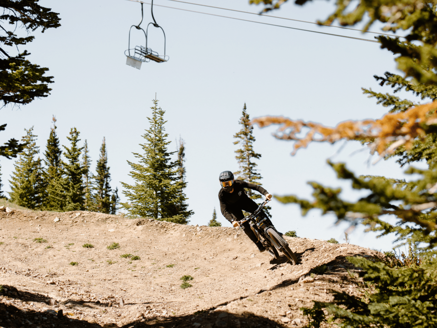 A person riding down a dirt trail on a mountain bike. A chairlift can be seen in the background.